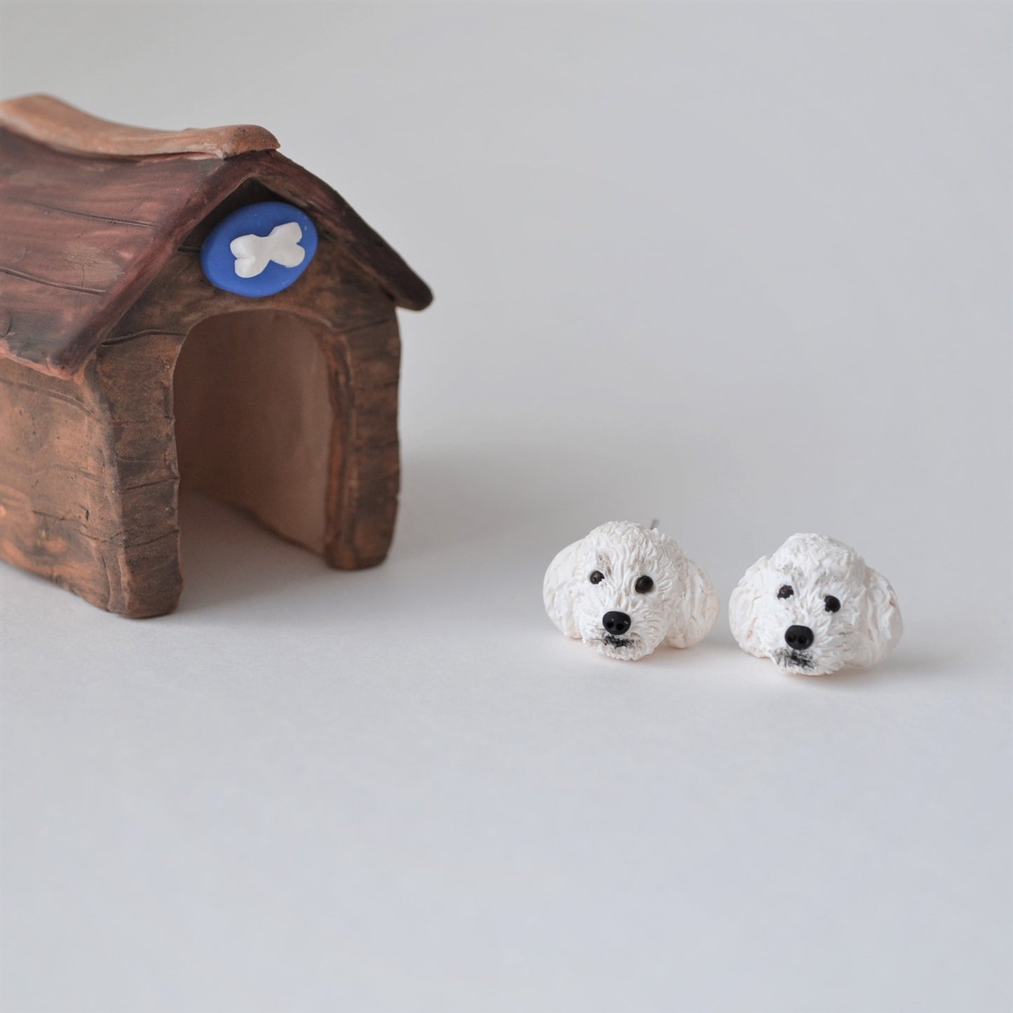 Handmade polymer clay white poodle stud earrings shown beside kennel