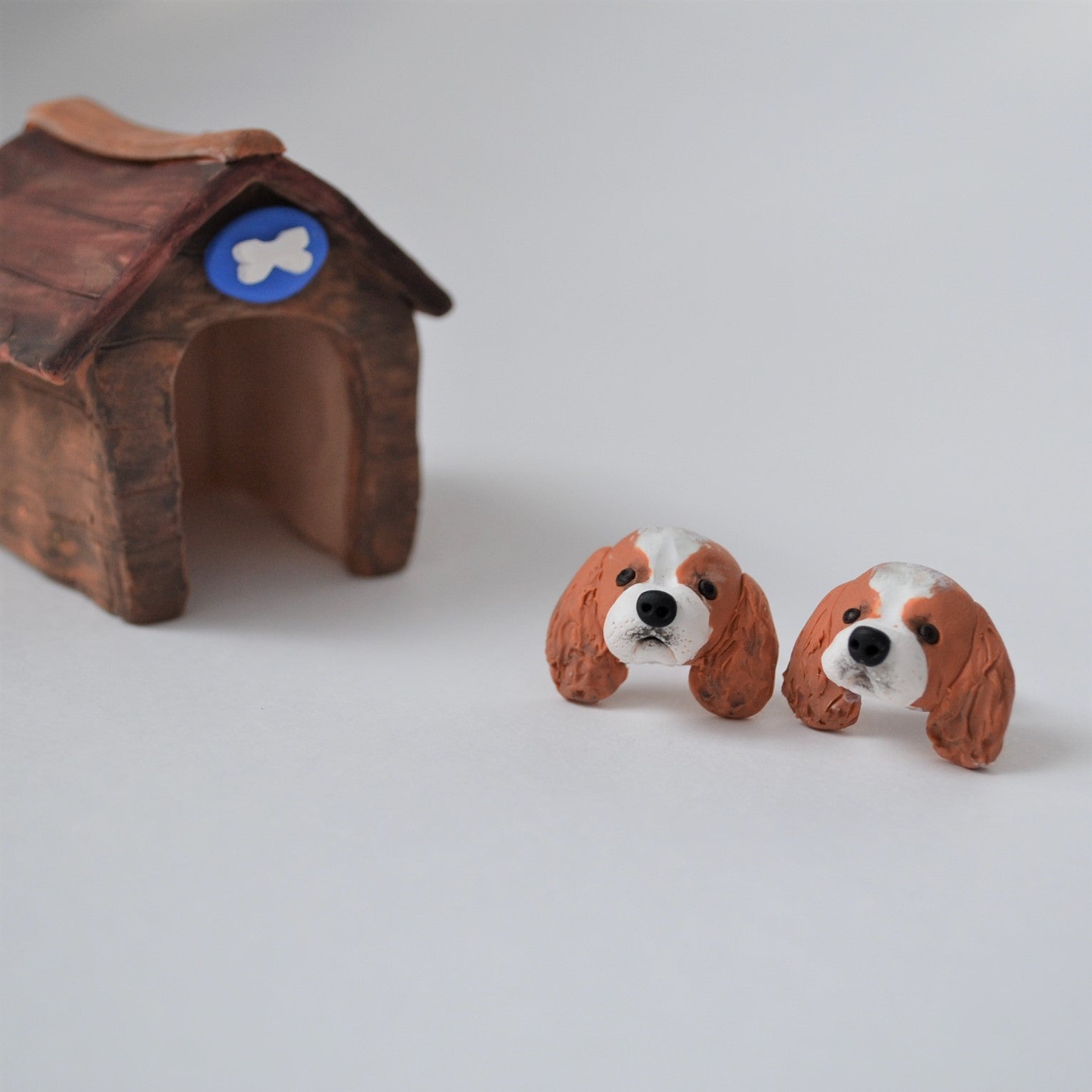 Handmade polymer clay Cavelier King Charles Spaniel stud earrings shown styled beside mini kennel