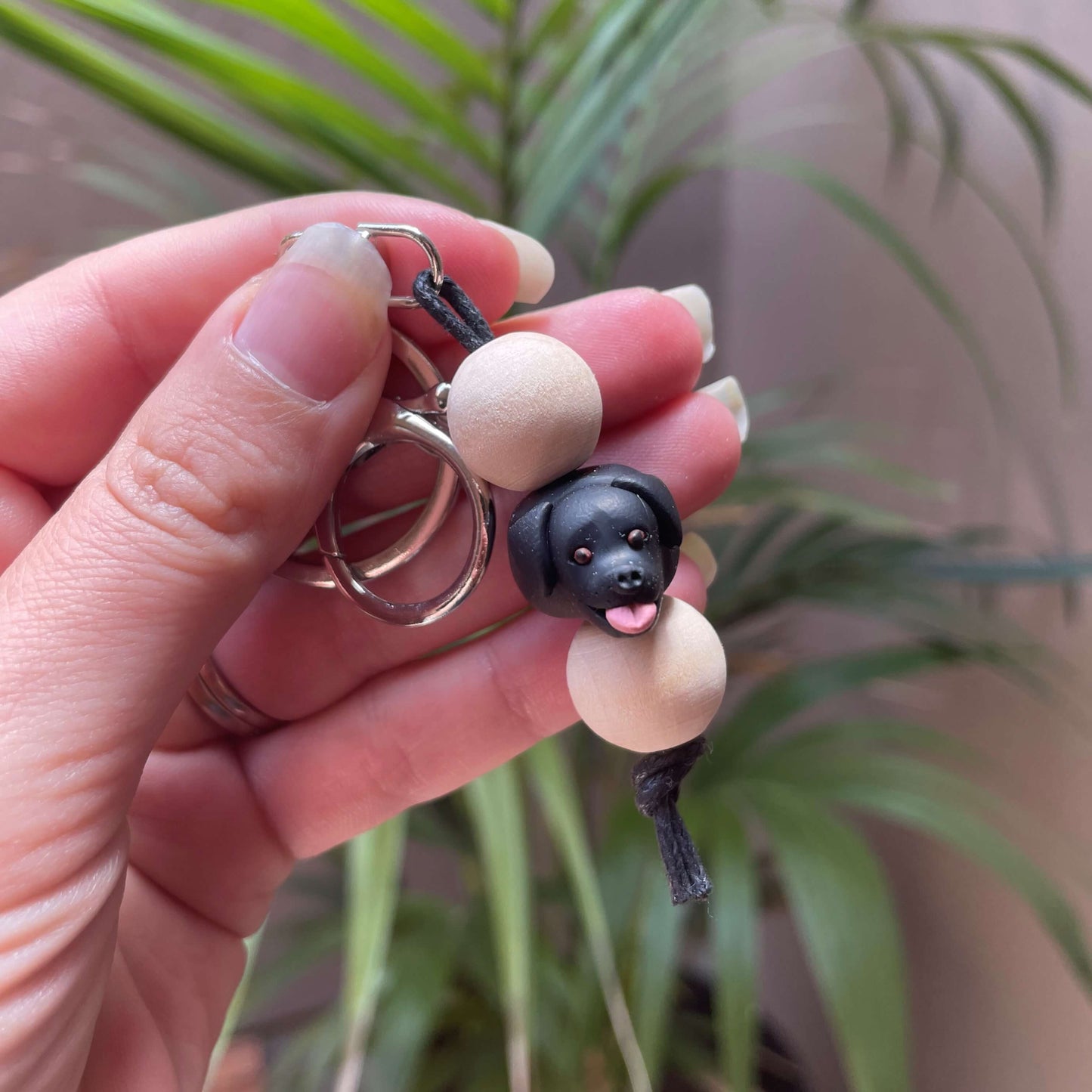 Handmade black labrador timber and polymer clay keychain being held in front of a green palm plant background