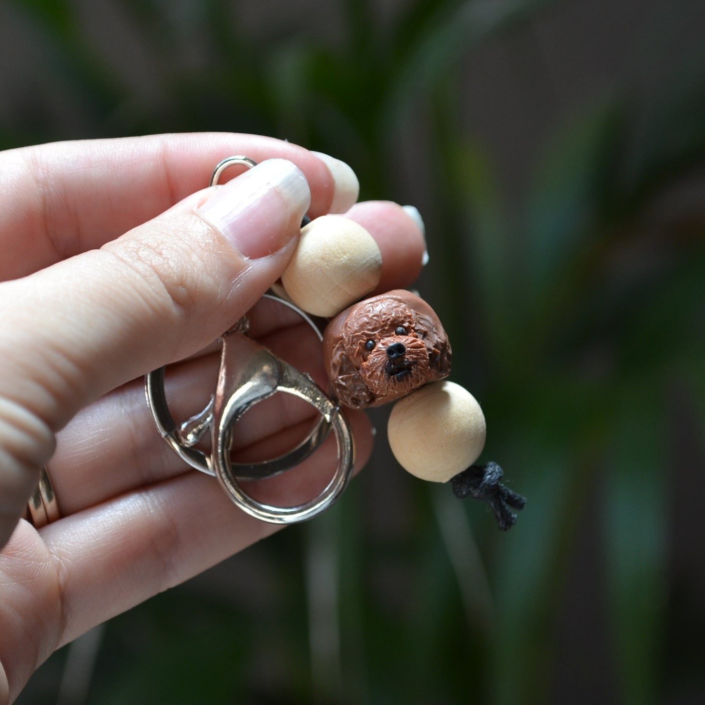 Handmade timber and polymer clay cavoodle dog keychain being held in front of green palm plant background
