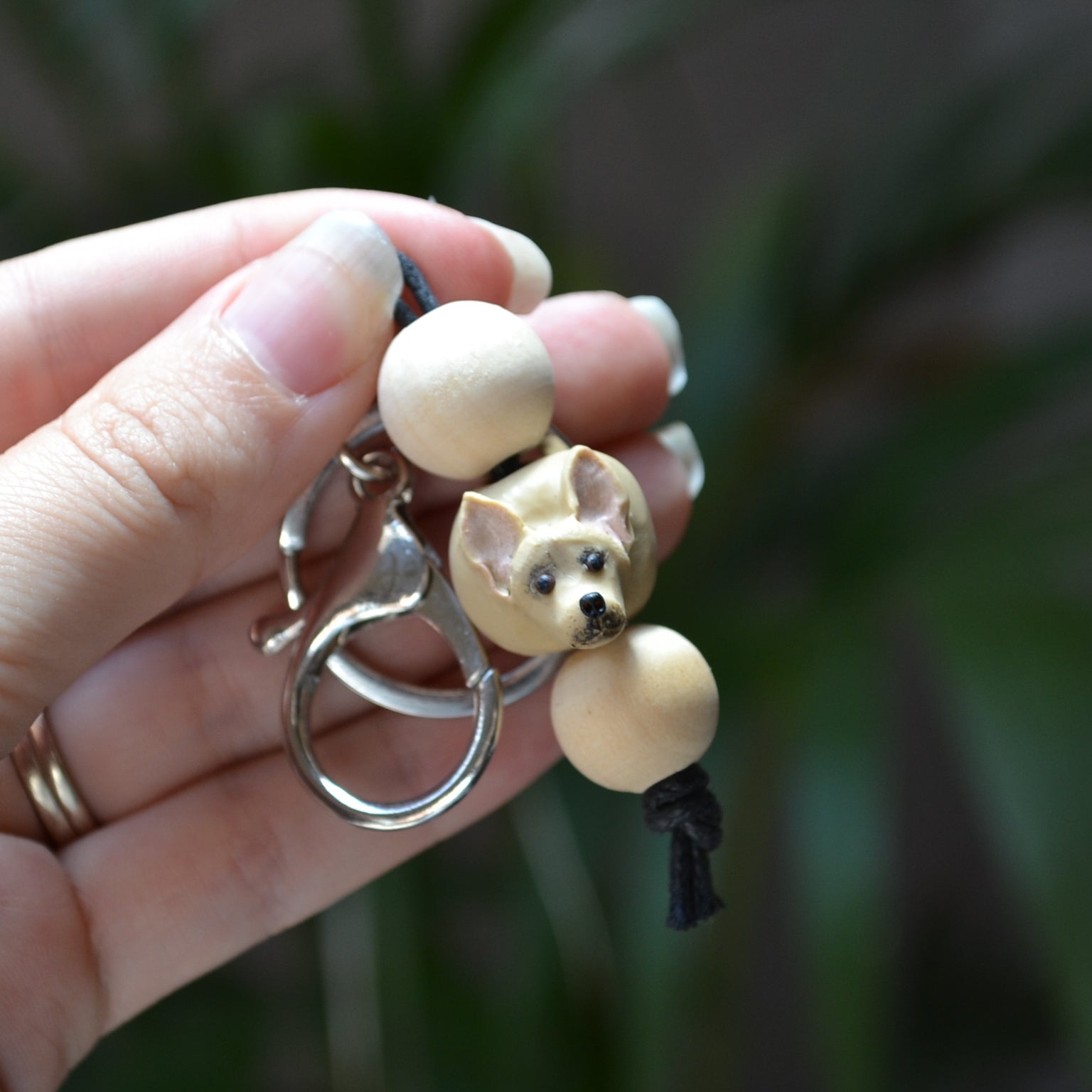 Handmade timber and polymer clay chihuahua dog keychain being held in front of green palm plant background