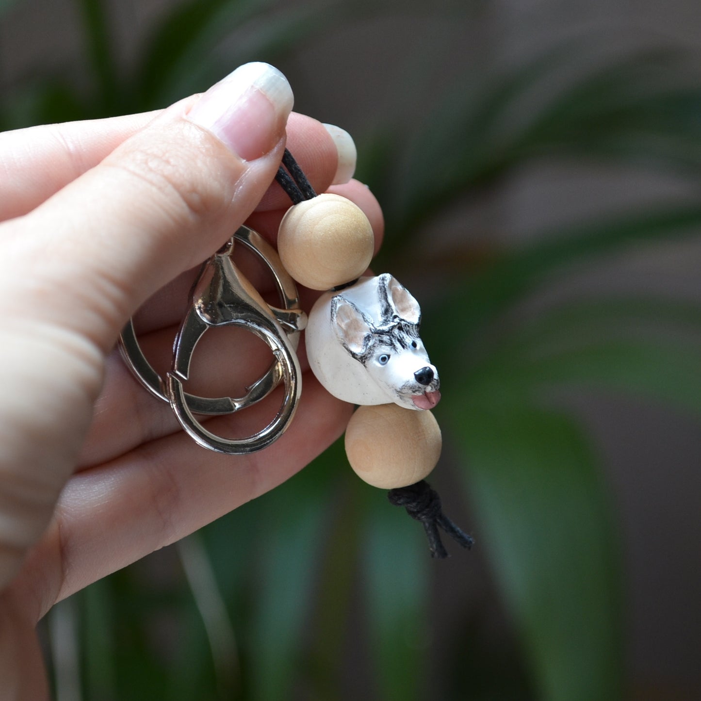 Handmade timber and polymer clay husky dog keychain being held in front of green palm plant background