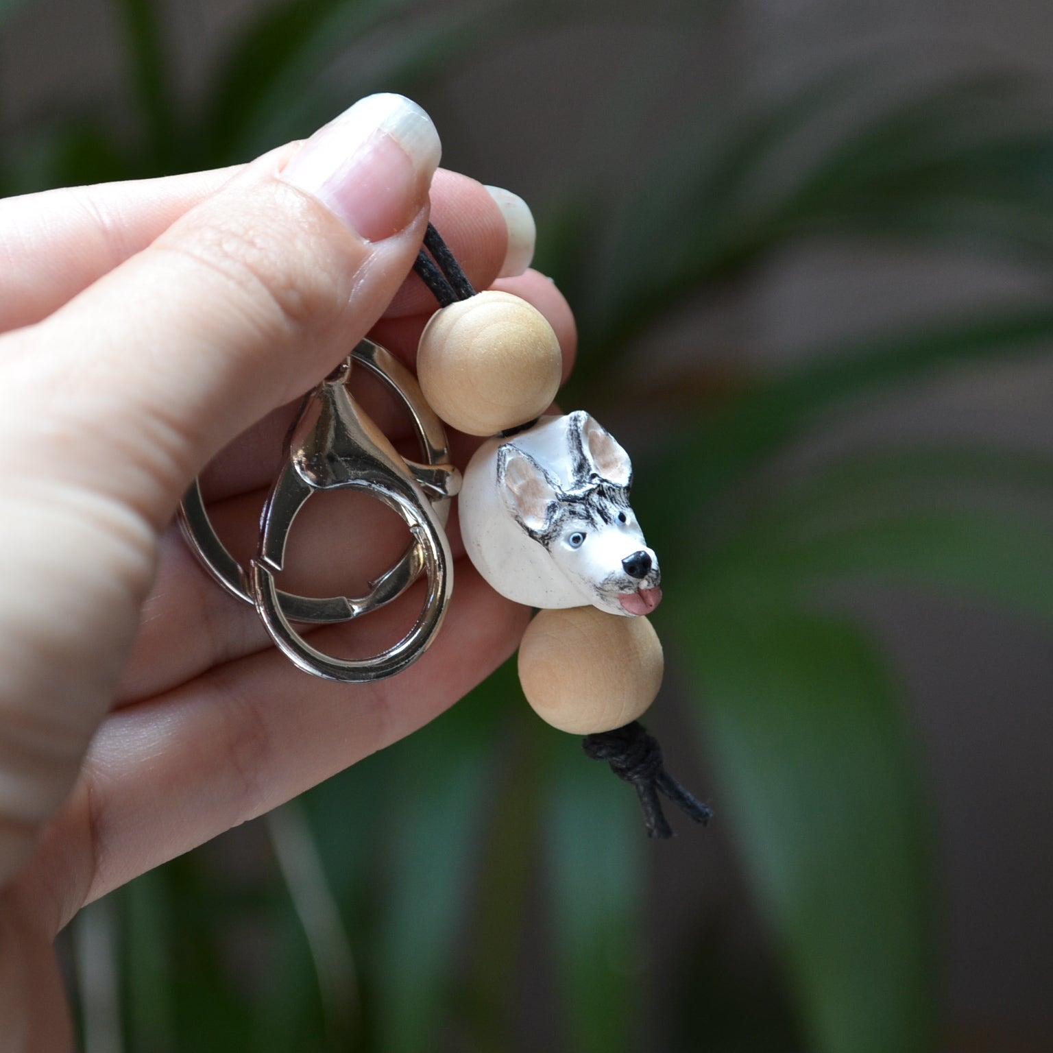 Handmade timber and polymer clay husky dog keychain being held in front of green palm plant background