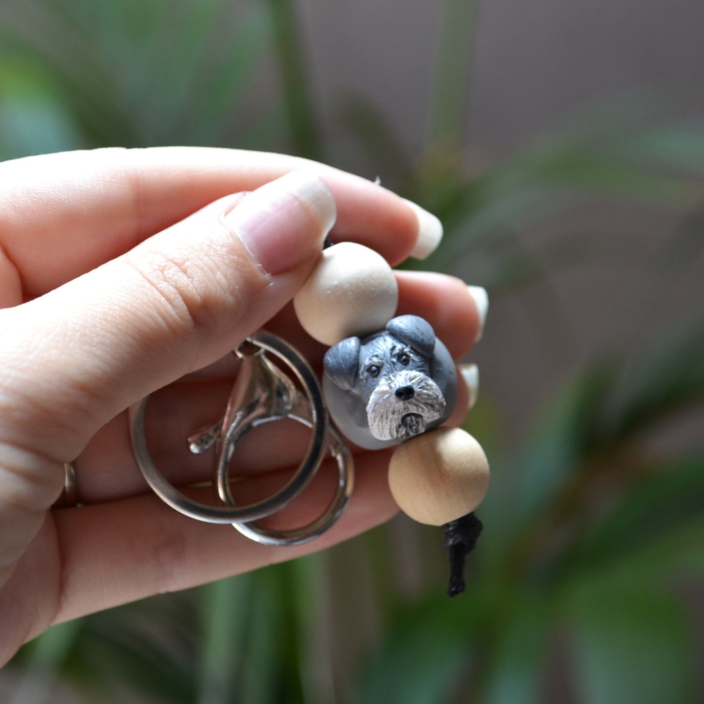 Handmade timber and polymer clay grey schnauzer dog keychain being held in front of green palm plant background