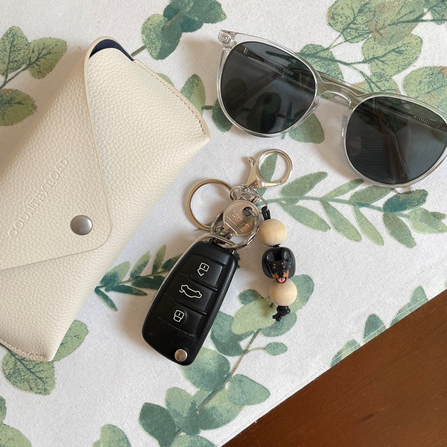 Polymer clay and timber handmade kelpie keyring on tablecloth beside sunglasses