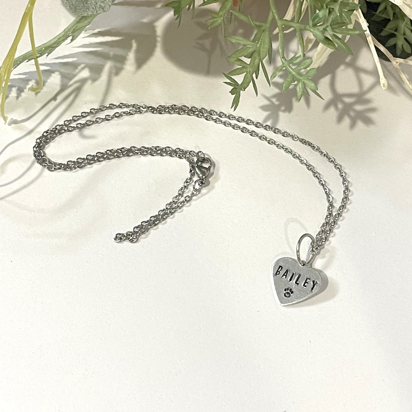 Metal hand-stamped bouquet pendant charm hanging on silver necklace chain, displaying the name Bailey.