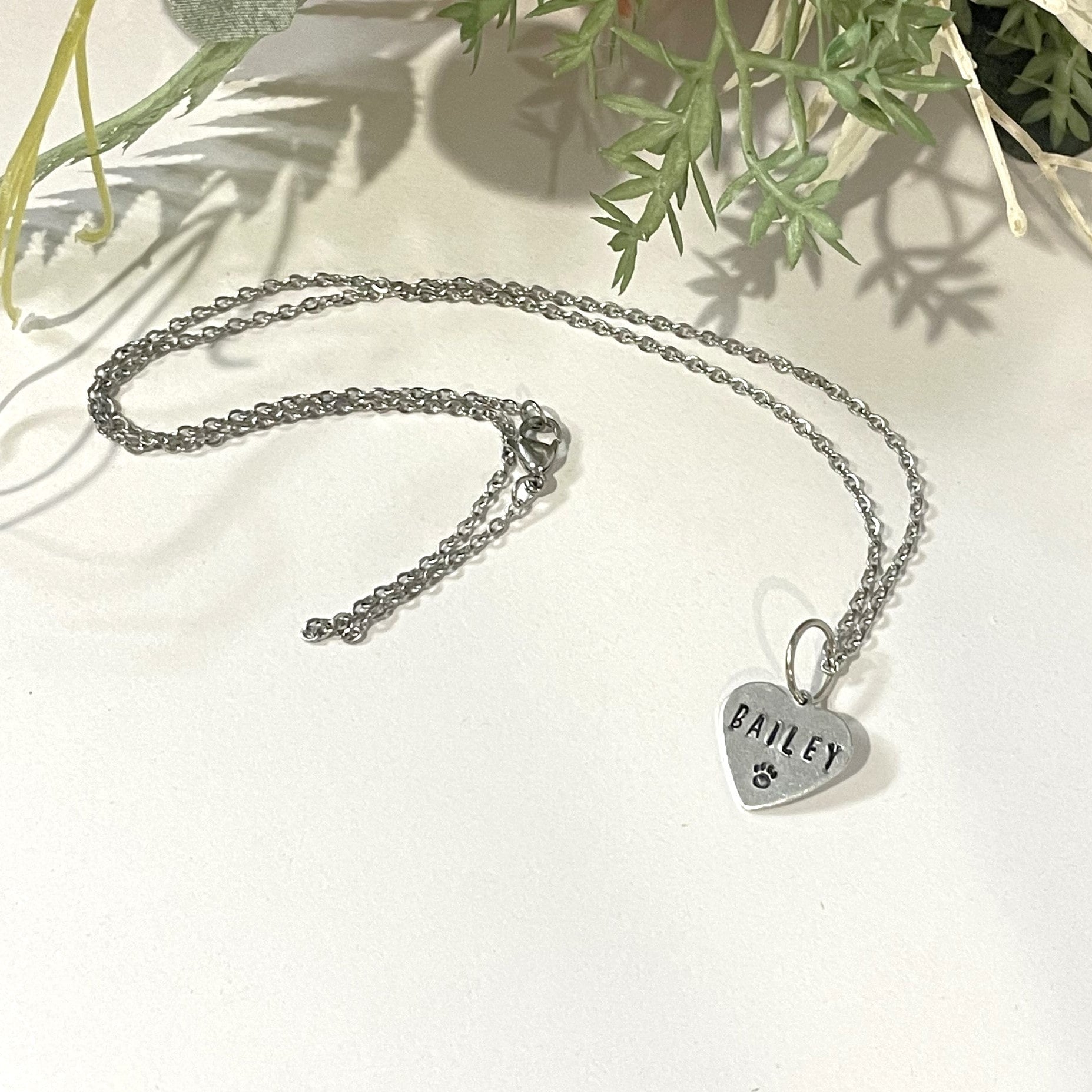 Metal hand-stamped bouquet pendant charm hanging on silver necklace chain, displaying the name Bailey.