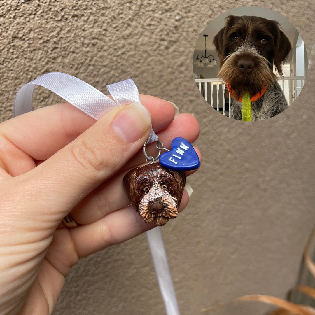 Handmade dog face pendant and blue heart charm, resembling a secondary photo of the dog. Pendants are hung on a ribbon intended to be placed on a wedding bouquet.