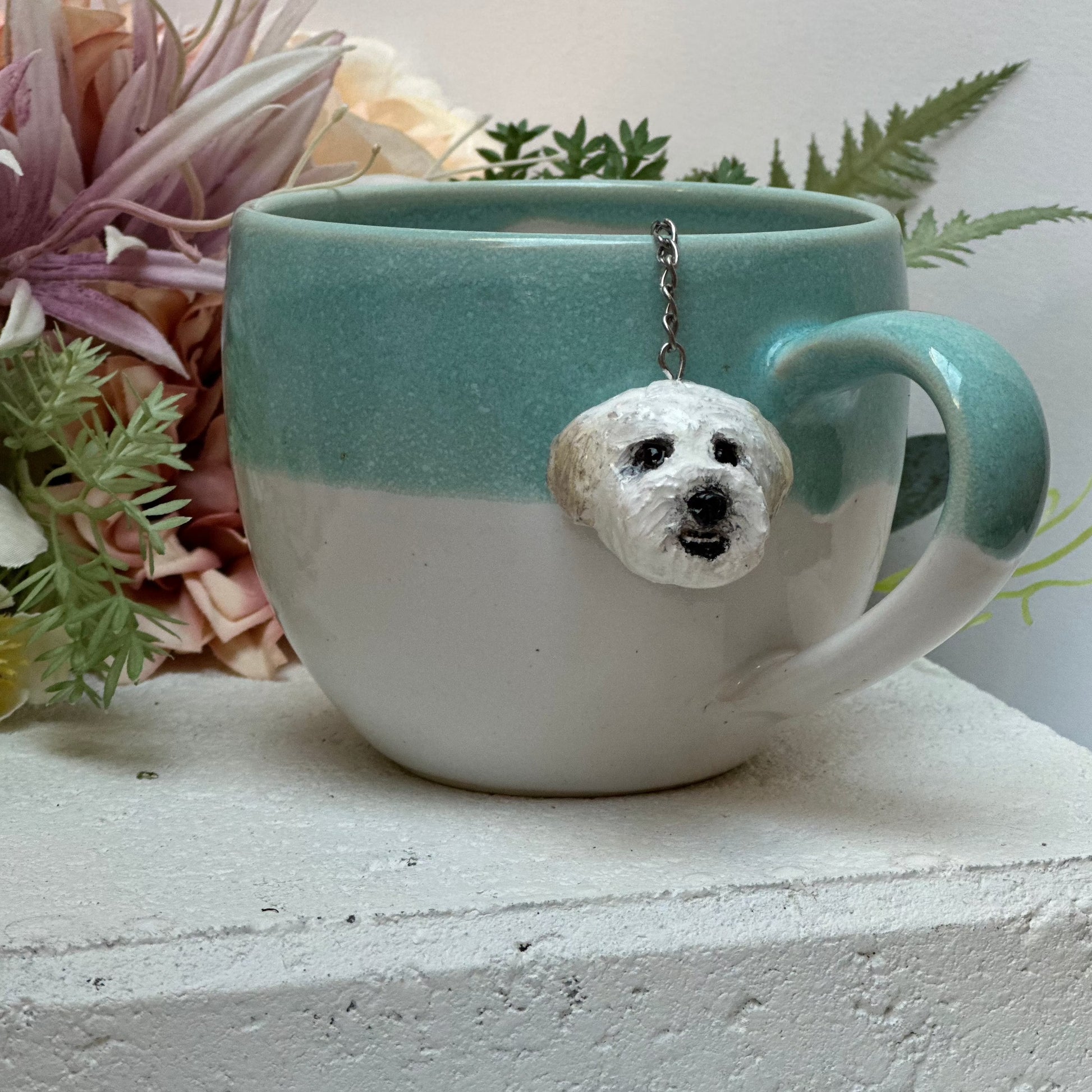 Handmade custom pet face mesh ball tea strainer being used in a teal mug.