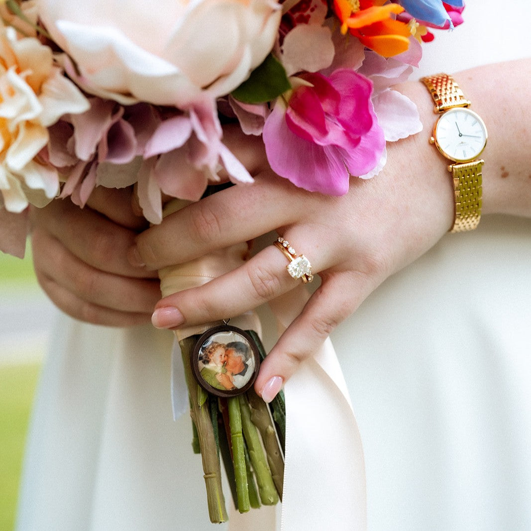 Close-up of hands holding a bouquet with a memorial charm attached.