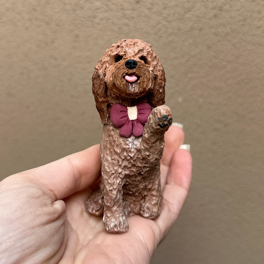 Small brown dog figurine with a pink bow tie held in a hand against a beige background