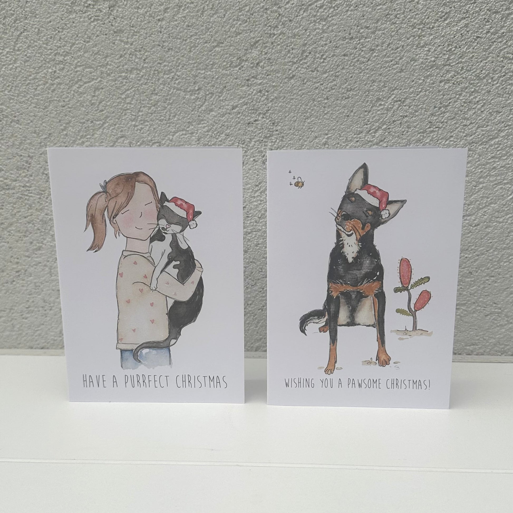 Two Christmas-themed greeting cards with illustrations of a girl and a dog on a textured gray background.