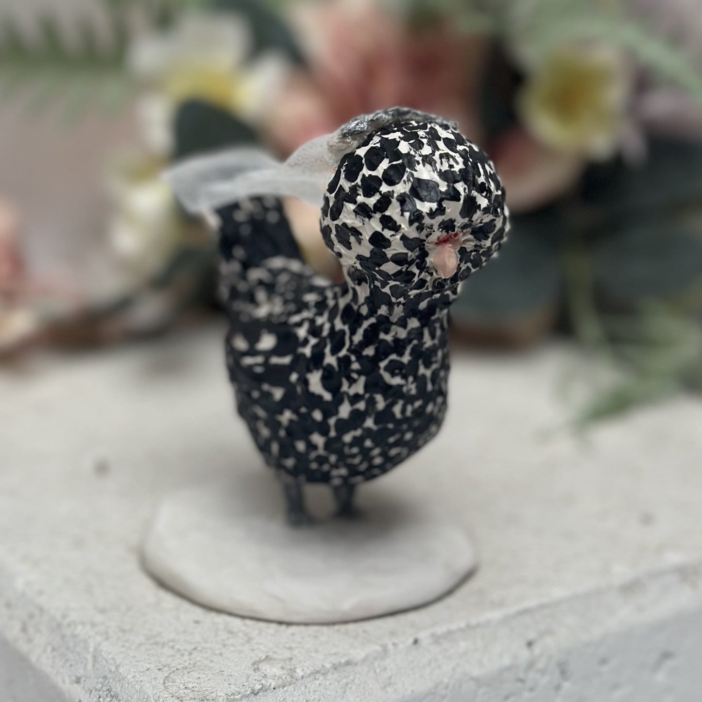 Small figurine of a bird with black and white pattern on a concrete surface.