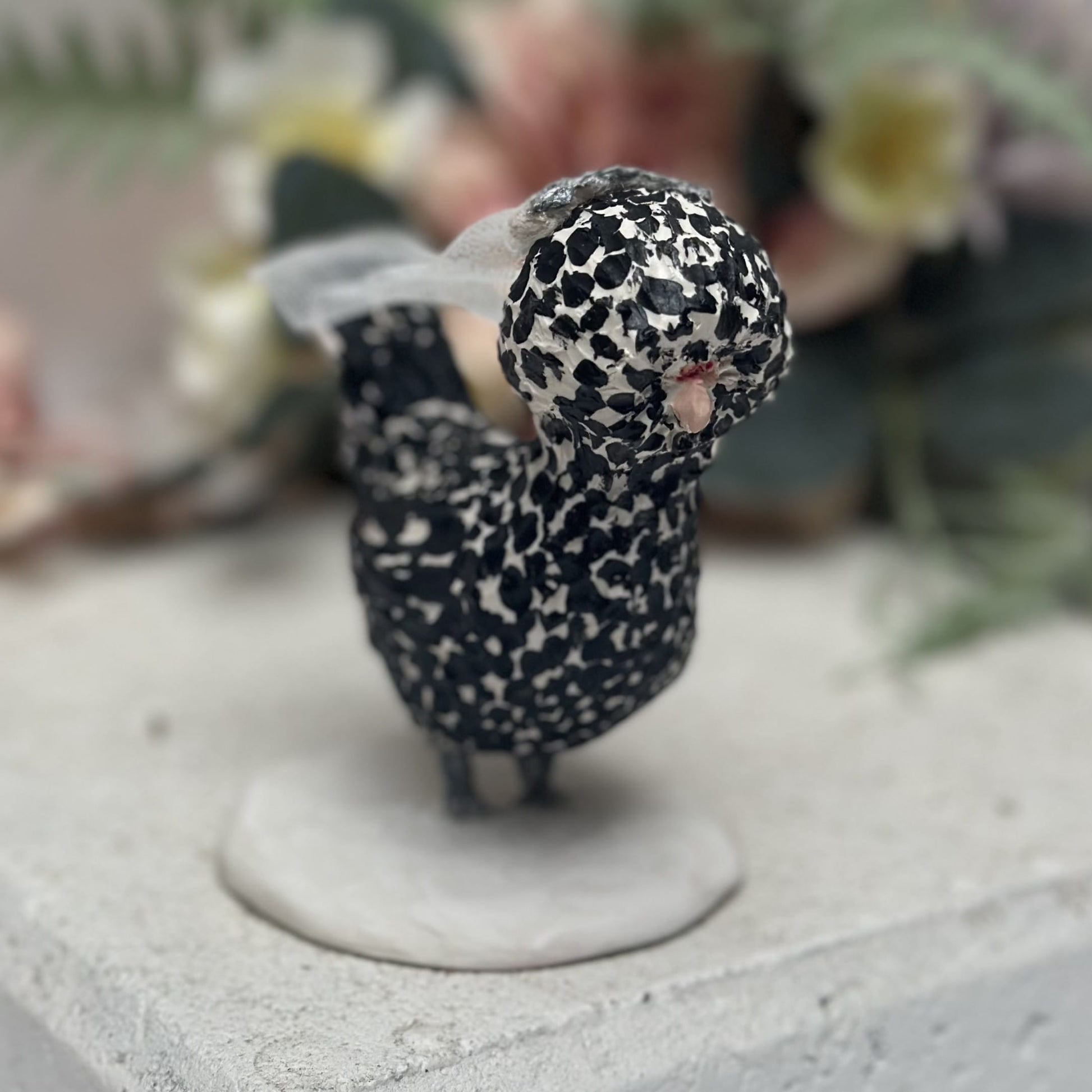 Small figurine of a bird with black and white pattern on a concrete surface.