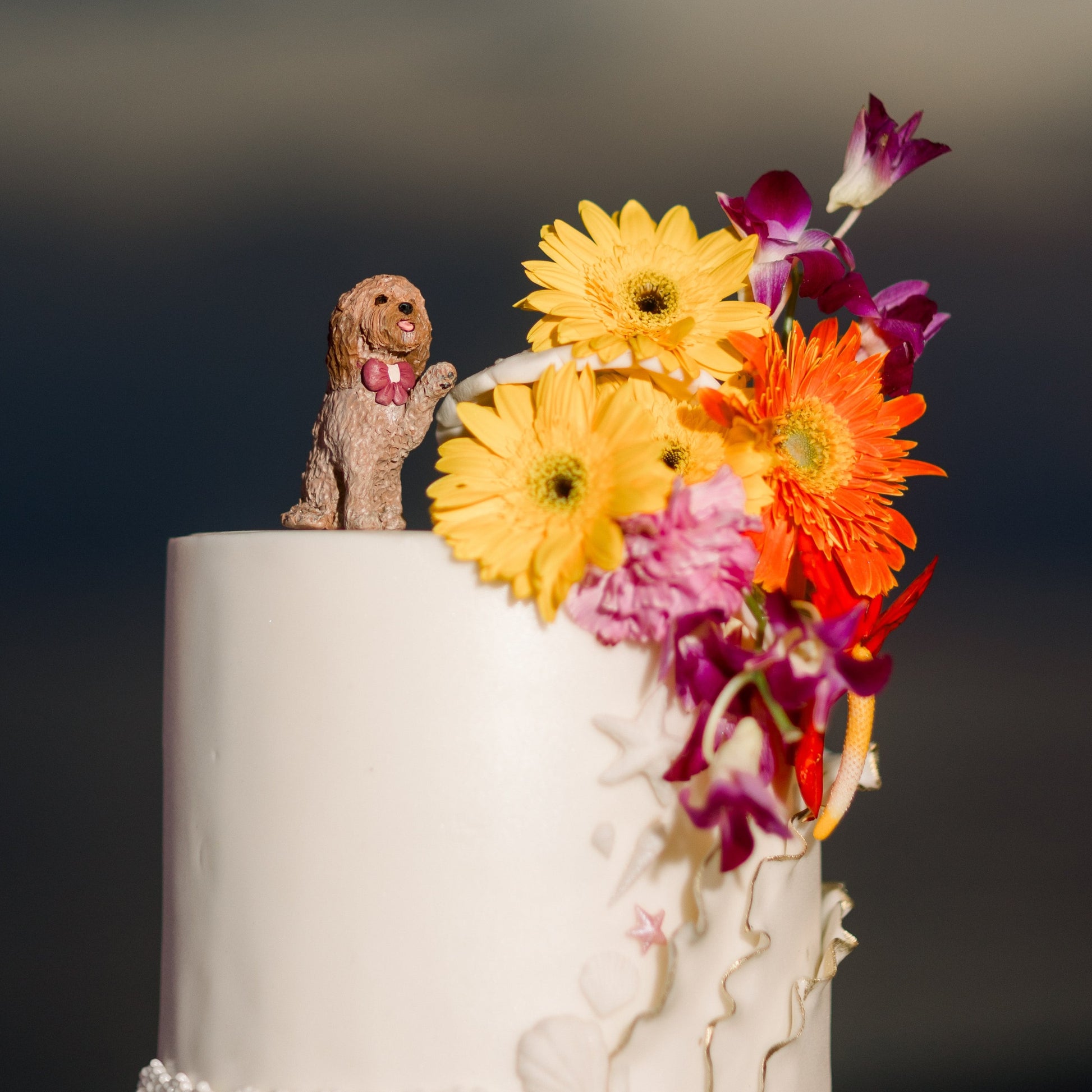 White cake with colorful flowers and a dog figurine on top against a dark background