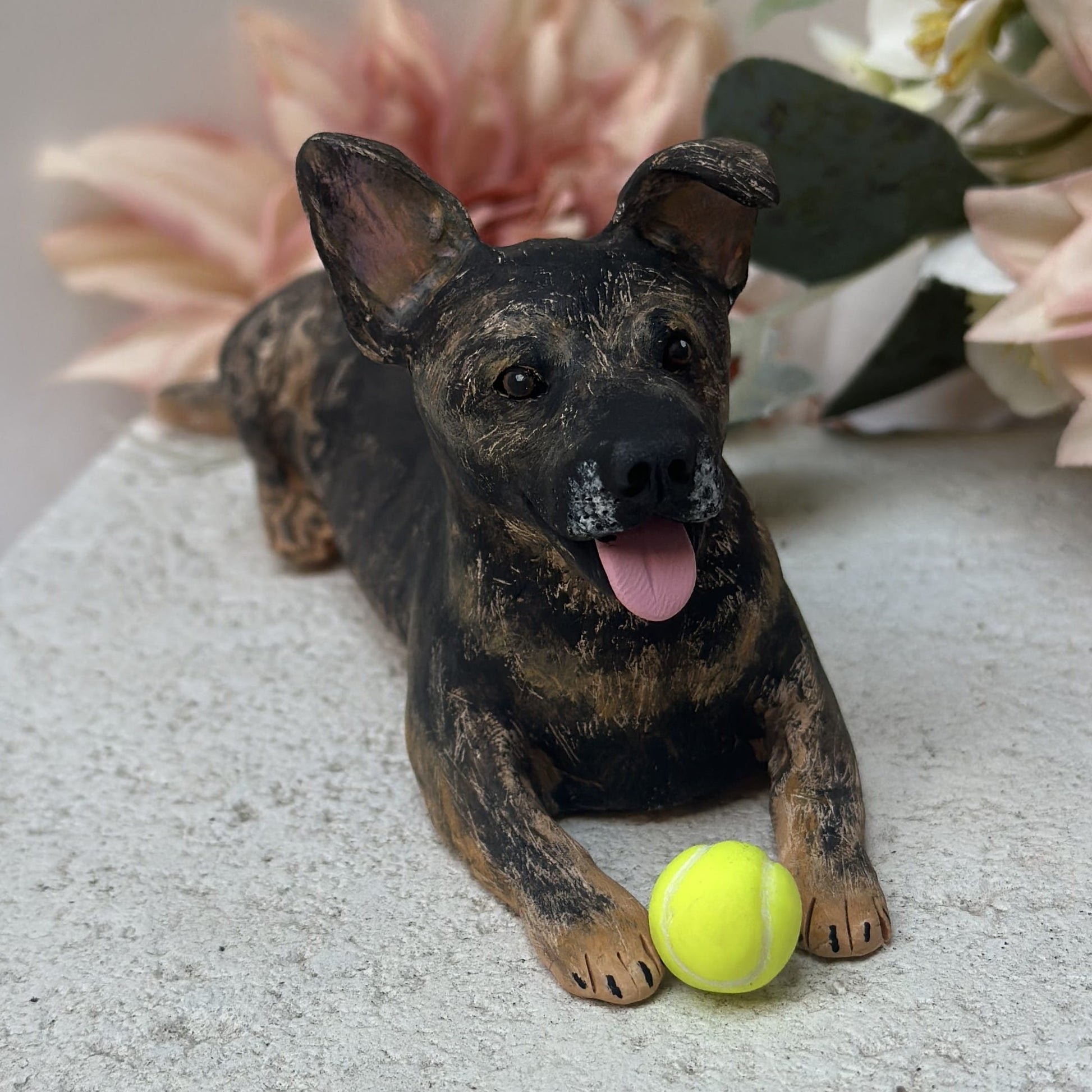 Dog figurine with a tennis ball on a textured surface with flowers in the background