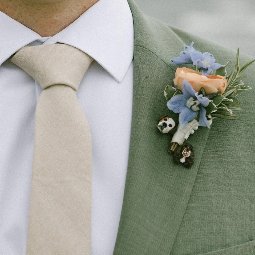 Green suit with a floral boutonniere and beige tie on a white background with 2 custom dog lapel pins
