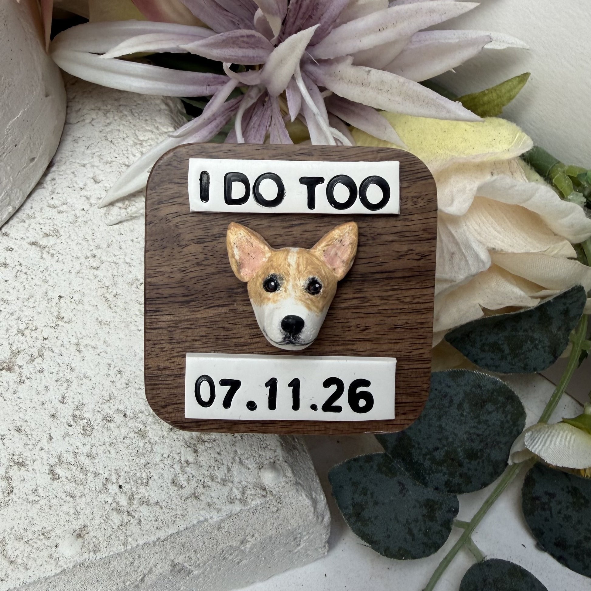 A square wooden wedding ring box, featuring a small sculpted dog face in the center and white labels with black text reading 'I DO TOO' at the top and '07.11.26'