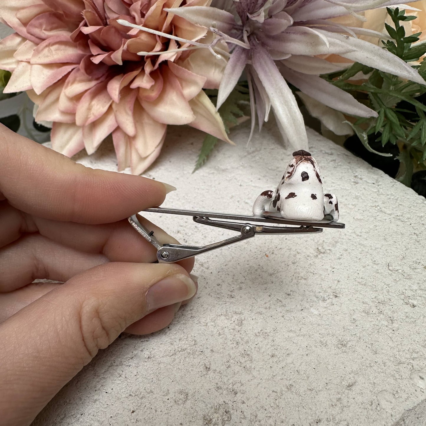Tie clip has a custom pet face feature being held by a hand with flowers in the background