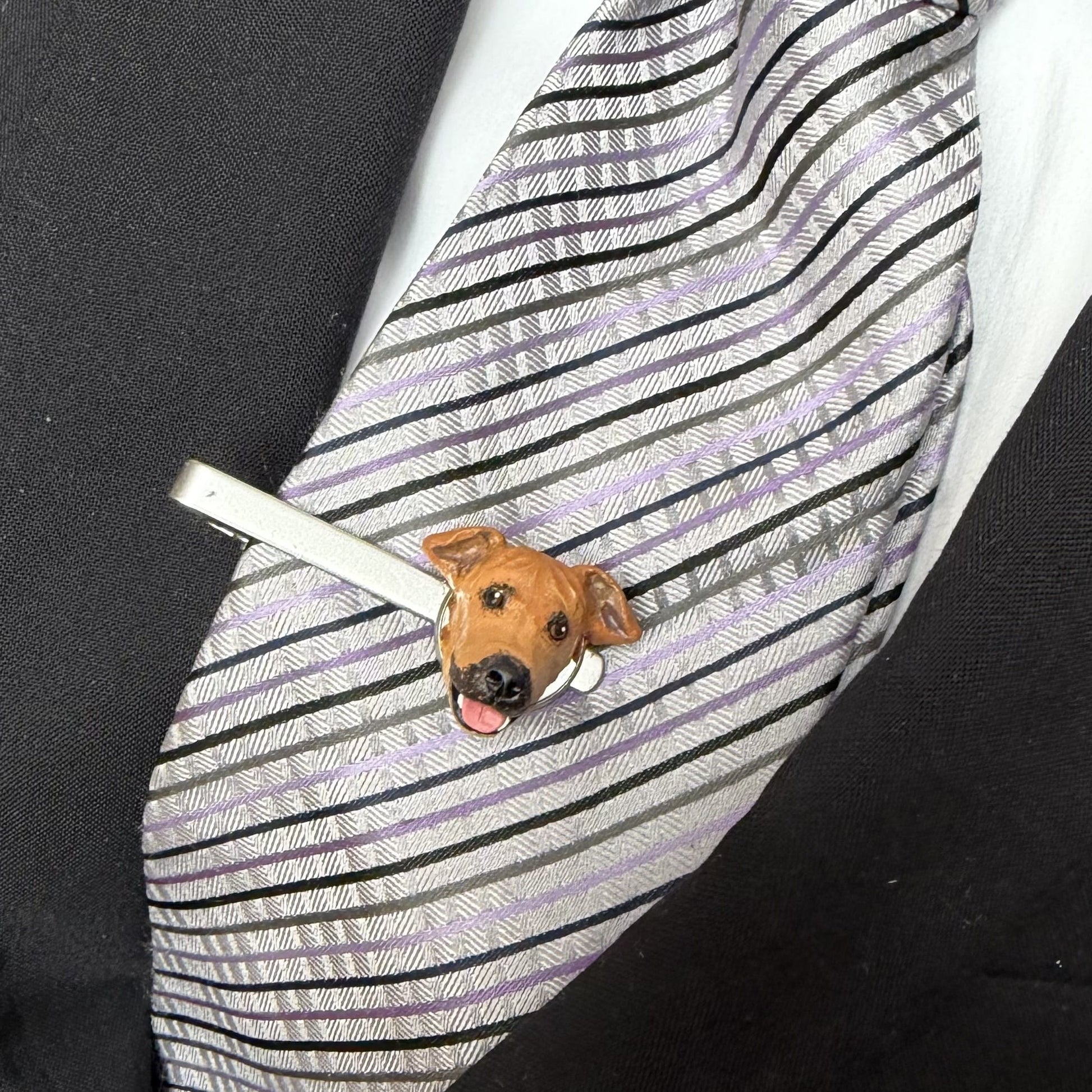 Tie clip with a dog design on a striped tie against a black background
