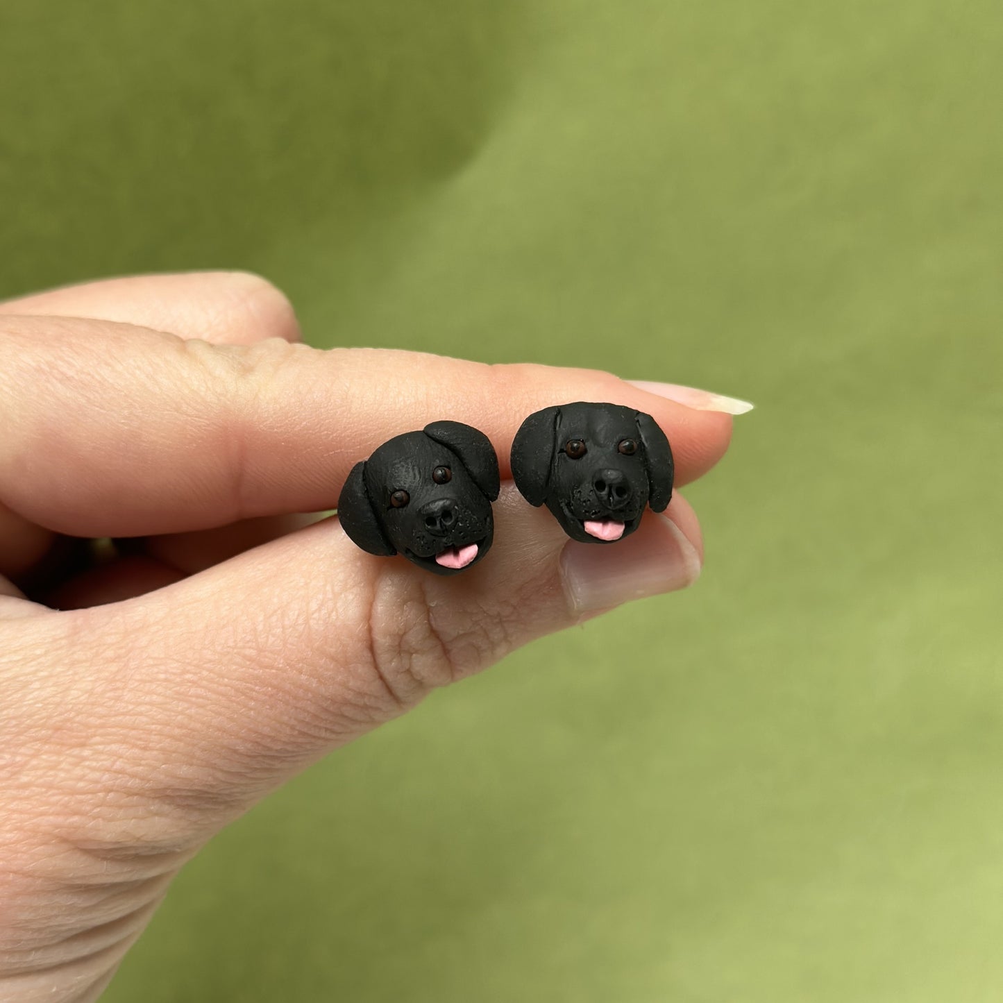 Handmade black labrador stud earrings by Pawfect Love, hold infront of green background