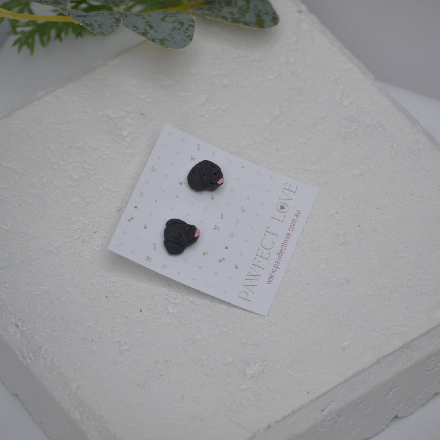 Handmade black labrador stud earrings by Pawfect Love, positioned on white paver background