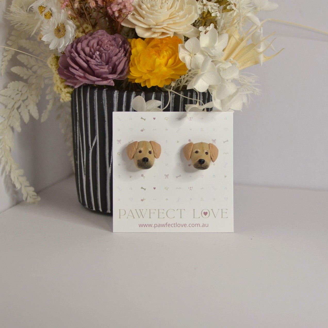 Handmade golden retriever stud earrings by Pawfect Love, positioned in front of dried flower arrangement