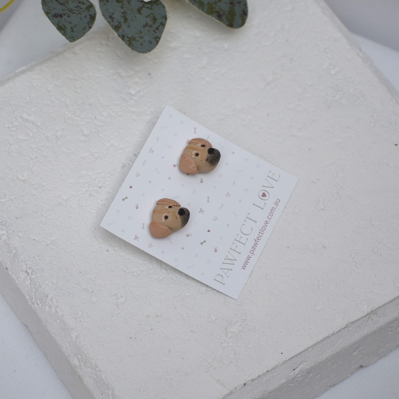 Handmade golden retriever stud earrings by Pawfect Love, positioned in front of white paver