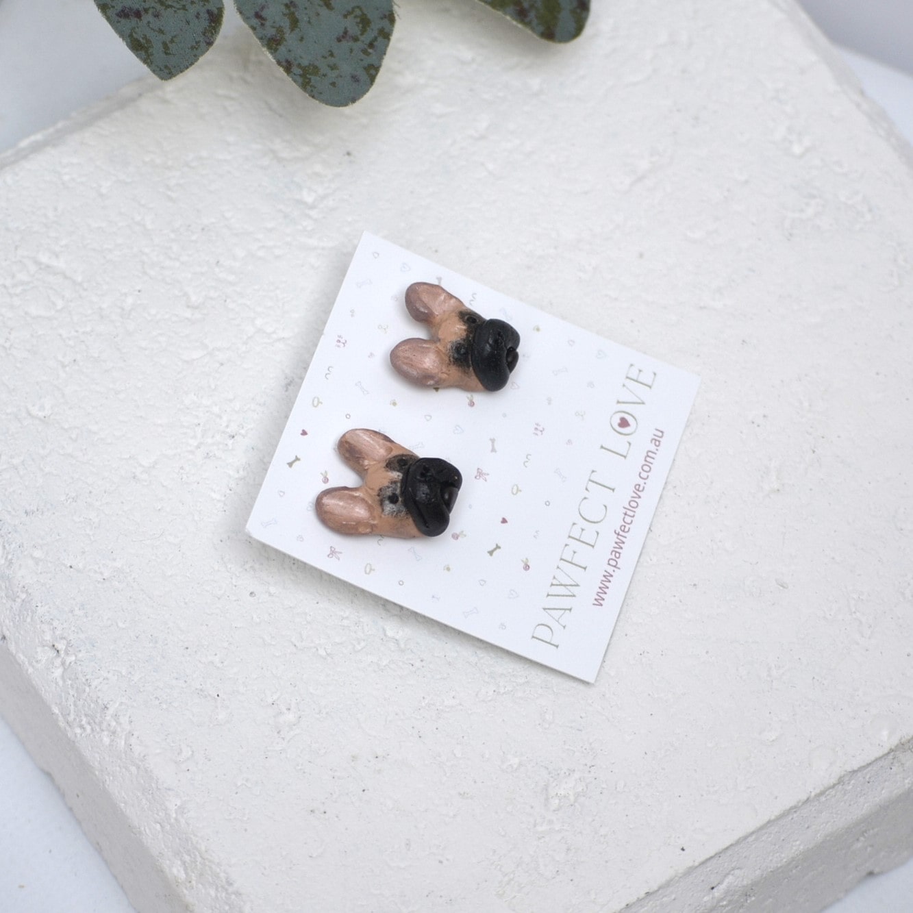 Handmade French bulldog stud earrings by Pawfect Love, positioned on white paver background