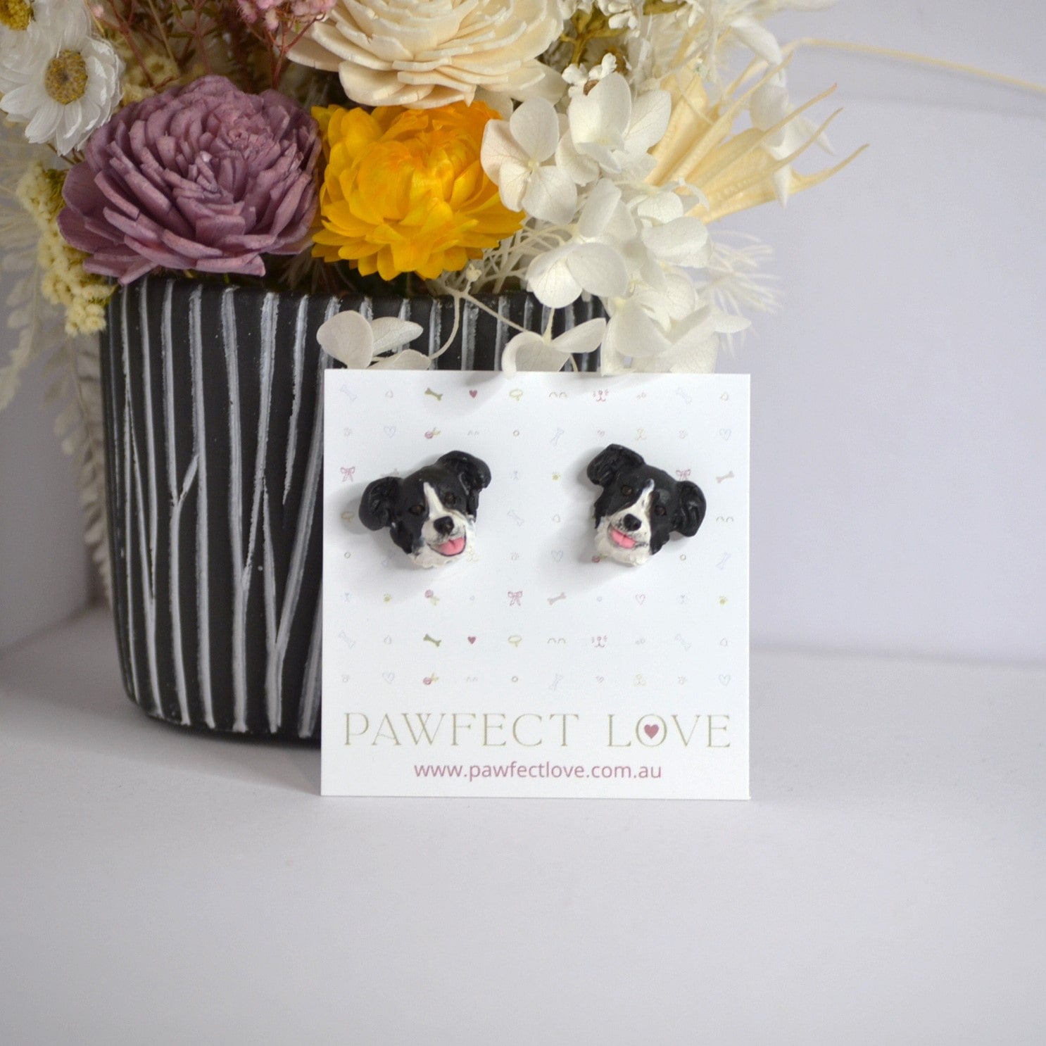 Handmade border collie stud earrings by Pawfect Love, positioned in front of dried flower arrangement