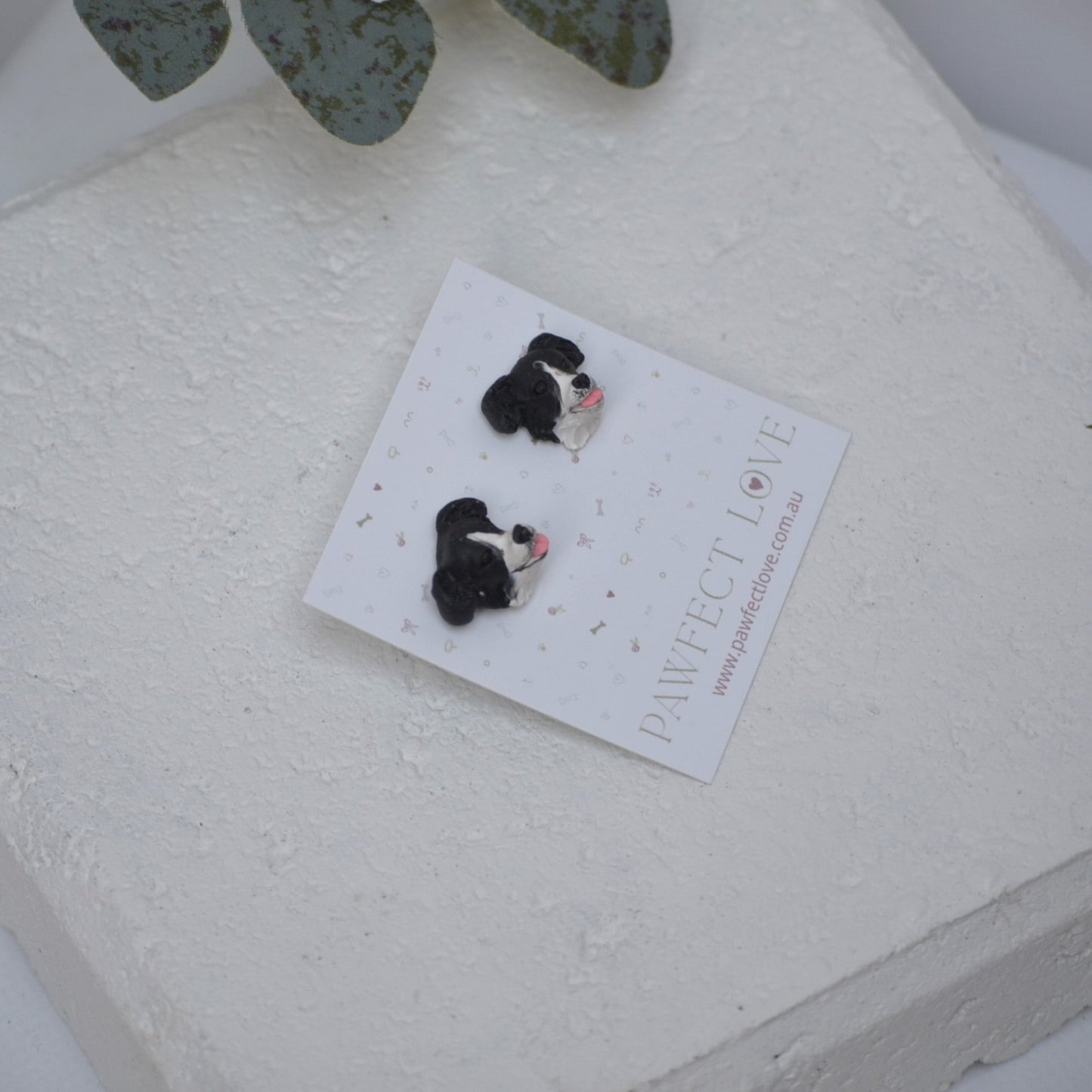 Handmade border collie stud earrings by Pawfect Love, positioned in front of white paver