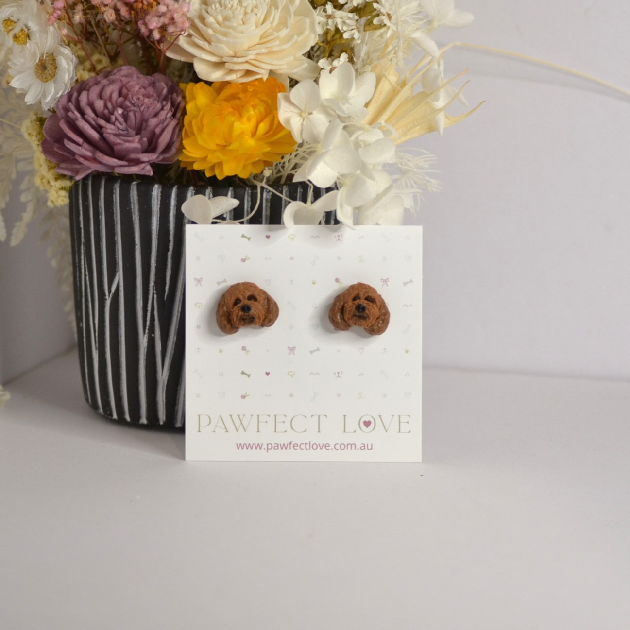 Handmade cavoodle stud earrings by Pawfect Love, positioned in front of dried flower arrangement