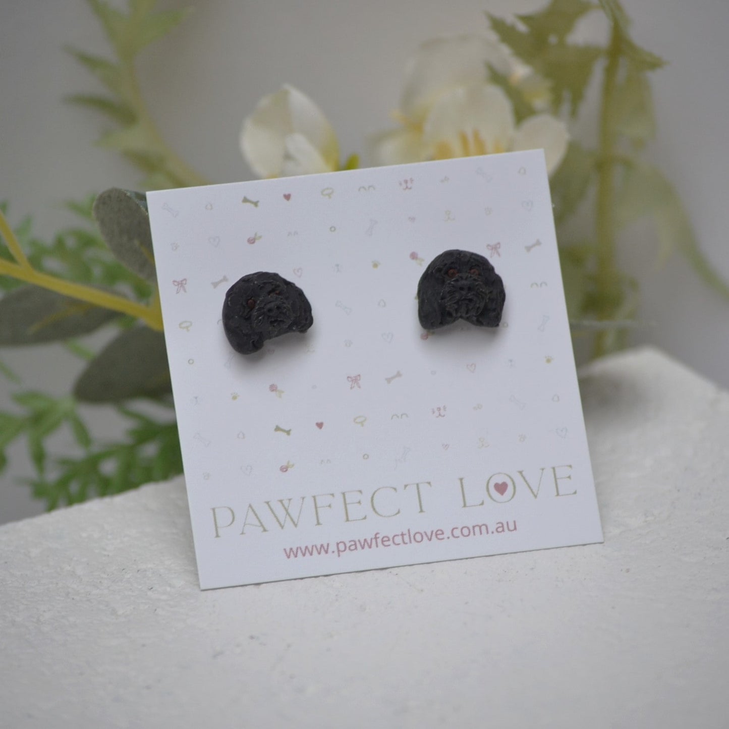 Handmade black poodle stud earrings by Pawfect Love, positioned in front of dried flower arrangement