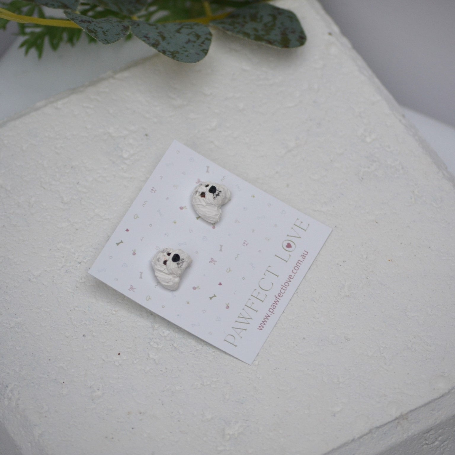 Handmade white poodle stud earrings by Pawfect Love, positioned in front of white paver