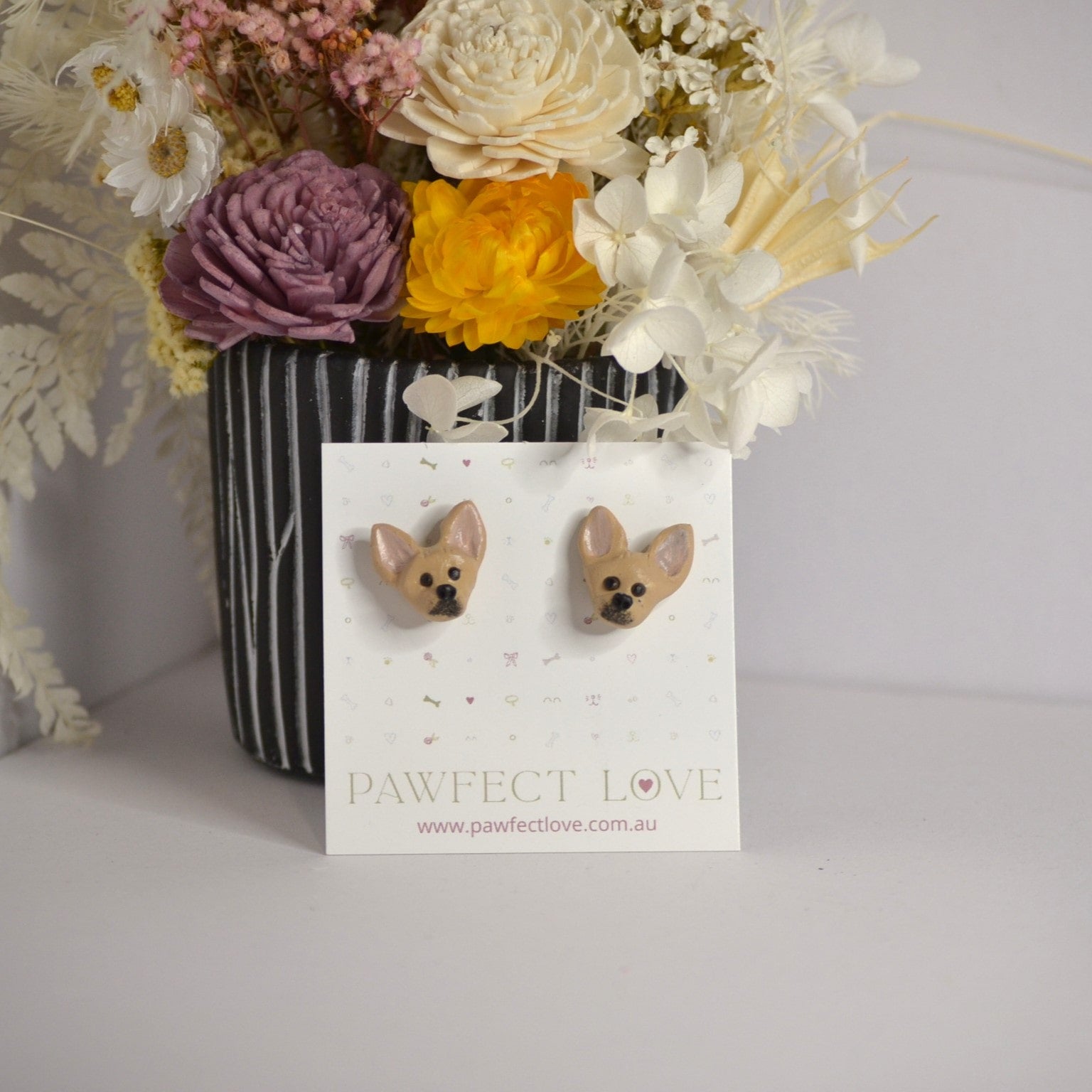 Handmade Chihuahua stud earrings by Pawfect Love, positioned in front of dried flower arrangement