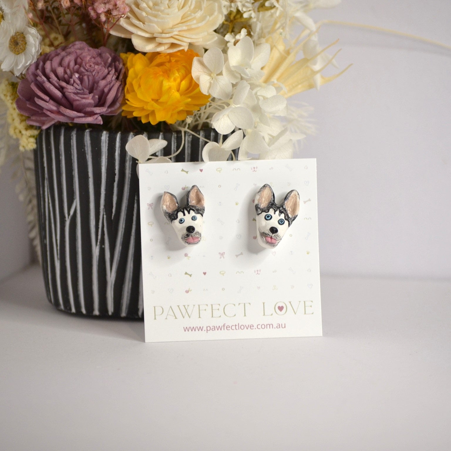 Handmade Husky stud earrings by Pawfect Love, positioned in front of dried flower arrangement