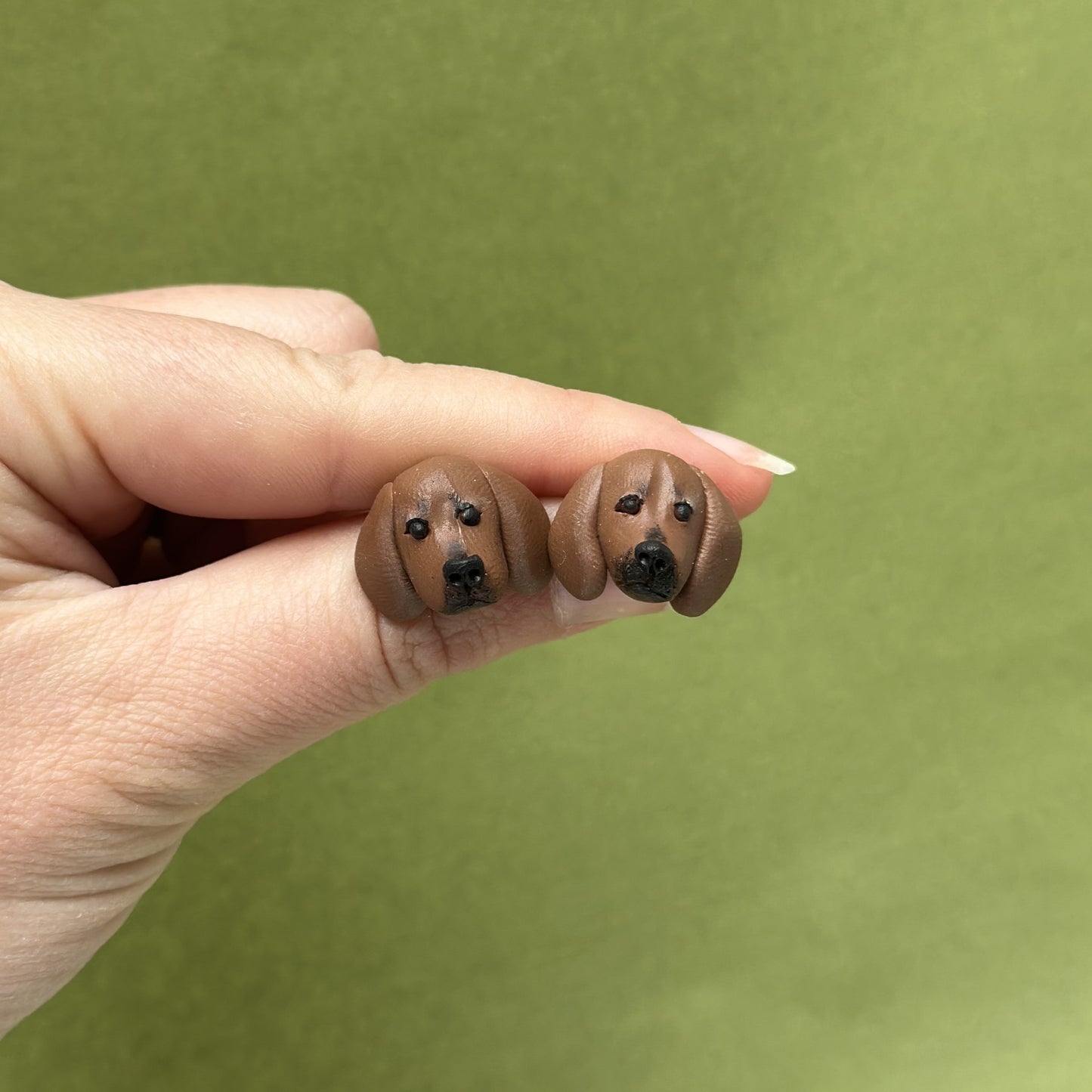 Handmade dachshund stud earrings by Pawfect Love, held over green background