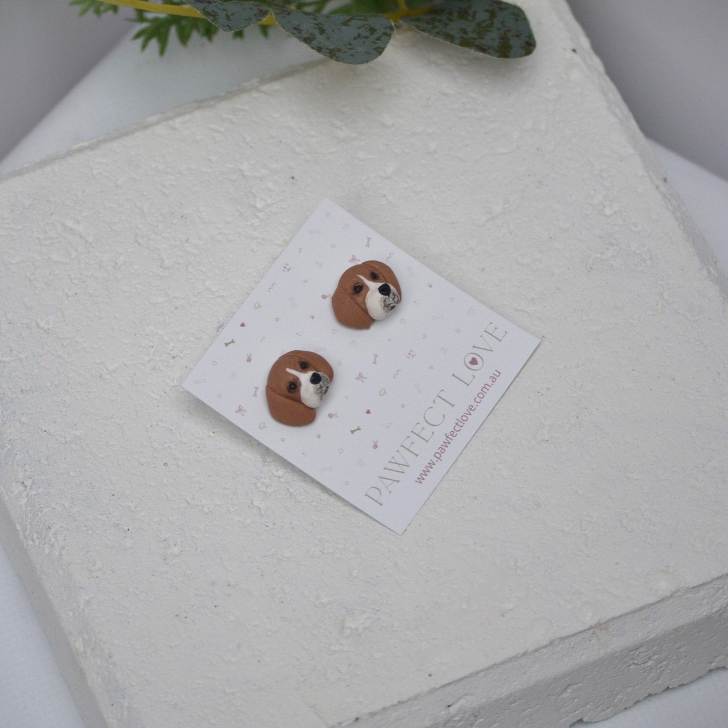 Handmade beagle stud earrings by Pawfect Love, positioned in front of white paver