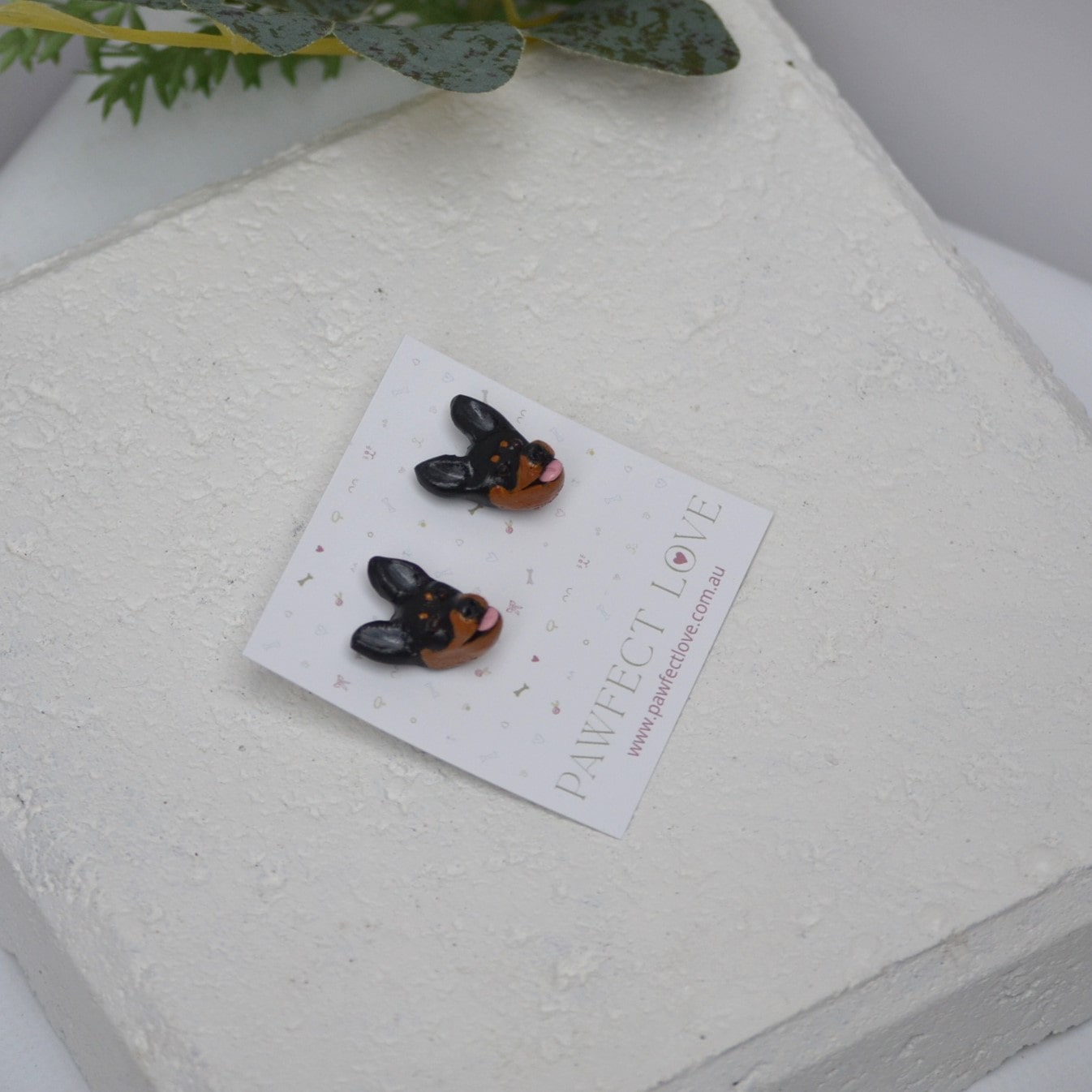 Handmade kelpie stud earrings by Pawfect Love, positioned in front of white paver