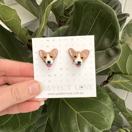 Card with corgi dog earrings held by a hand against a leafy green background