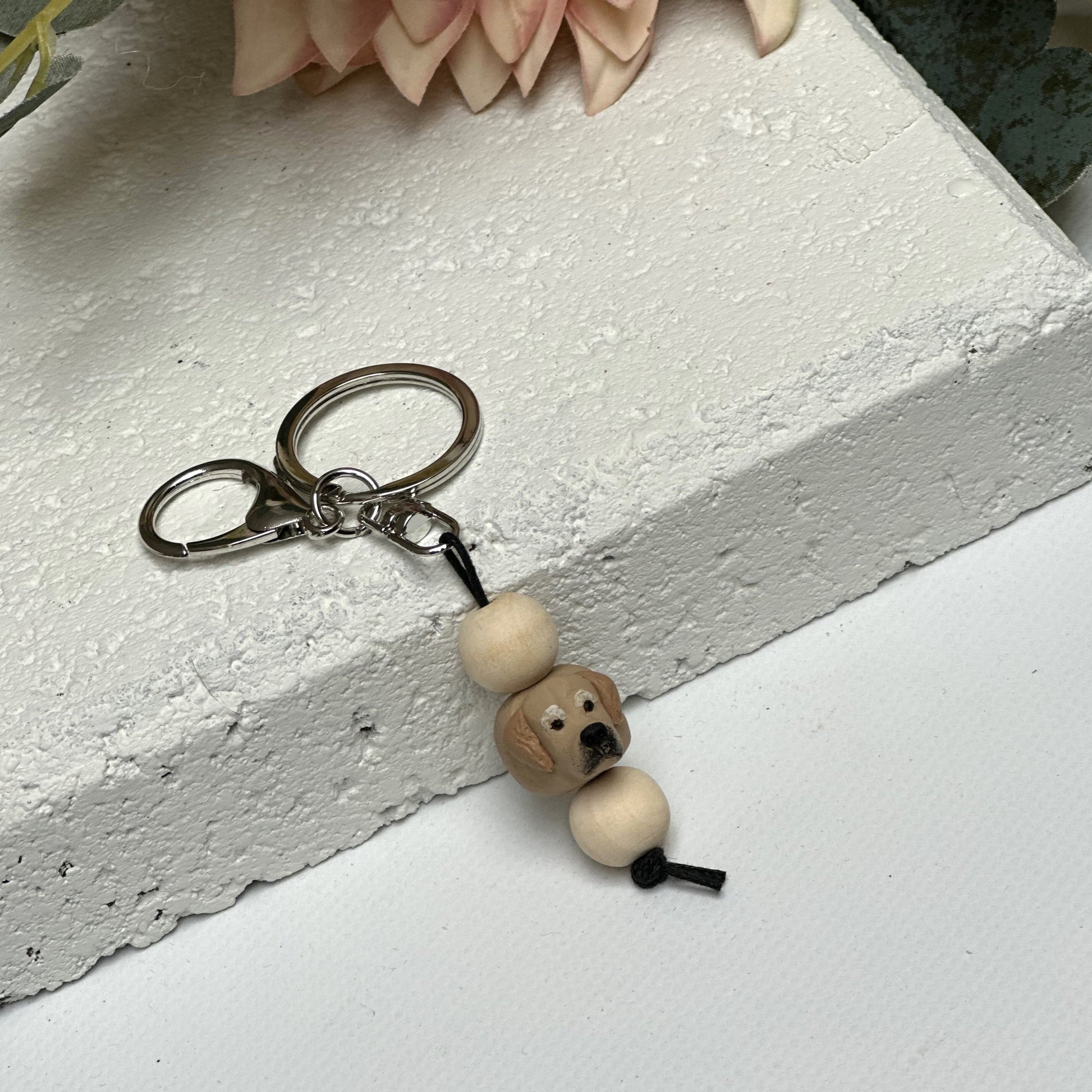 Handmade golden retriever dog polymer clay and timber keying on white textured background with a pink flower in the background