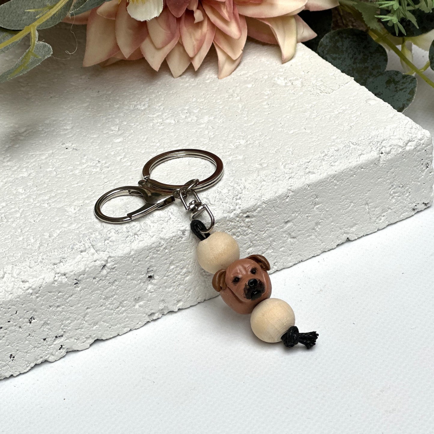 Handmade Staffy dog polymer clay and timber keying on white textured background with a pink flower in the background