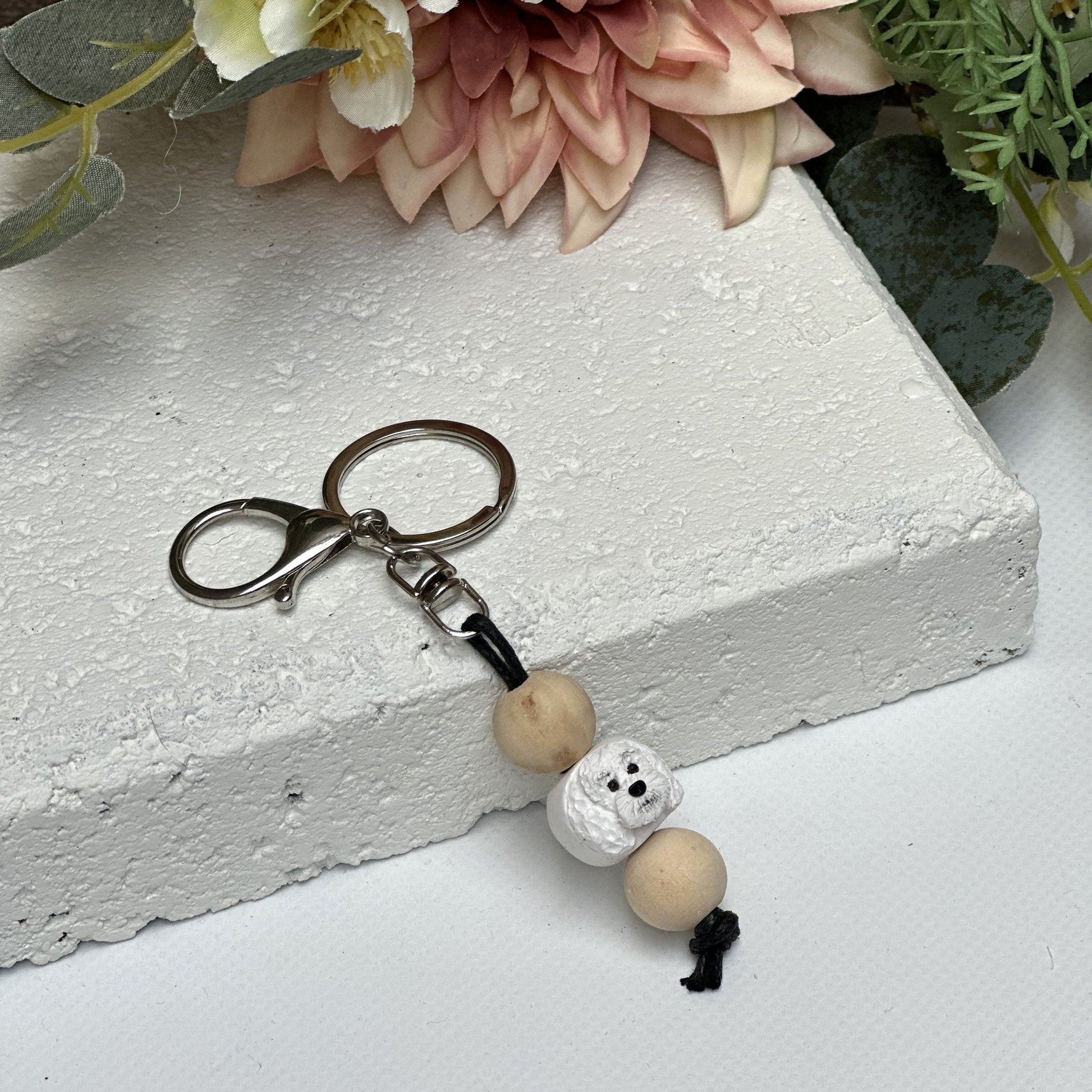 Handmade White Poodle dog polymer clay and timber keying on white textured background with a pink flower in the background
