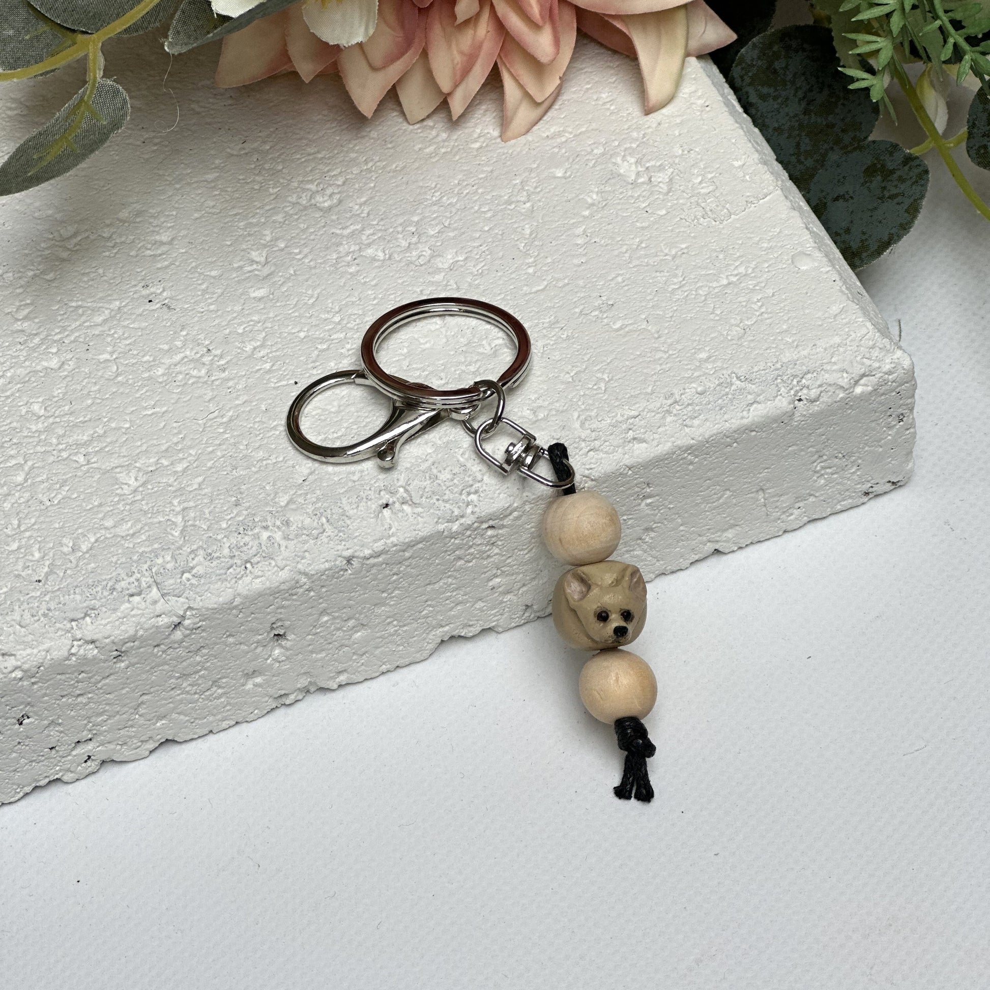Handmade chihuahua dog polymer clay and timber keying on white textured background with a pink flower in the background