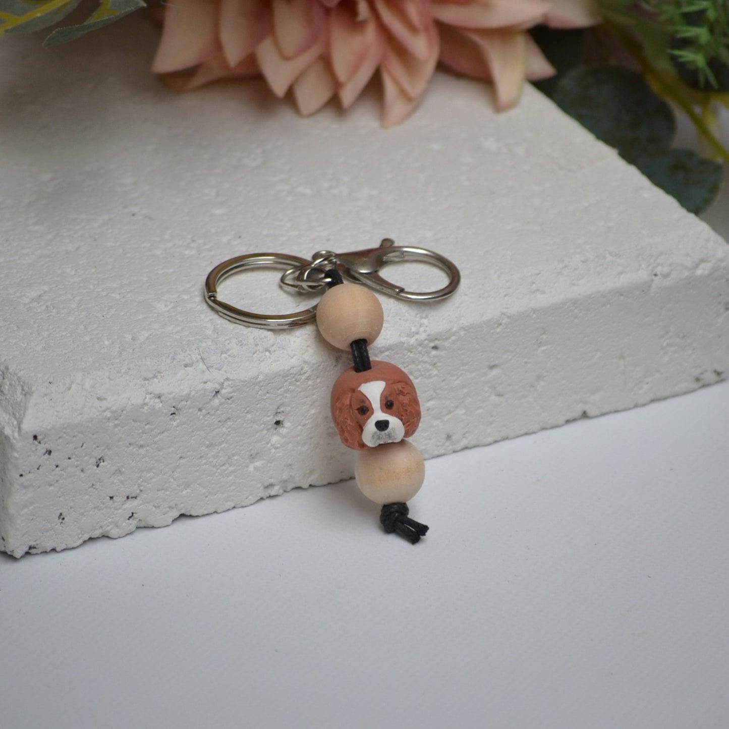 Handmade cavalier king charles spaniel polymer clay and timber keying on white textured background with a pink flower in the background