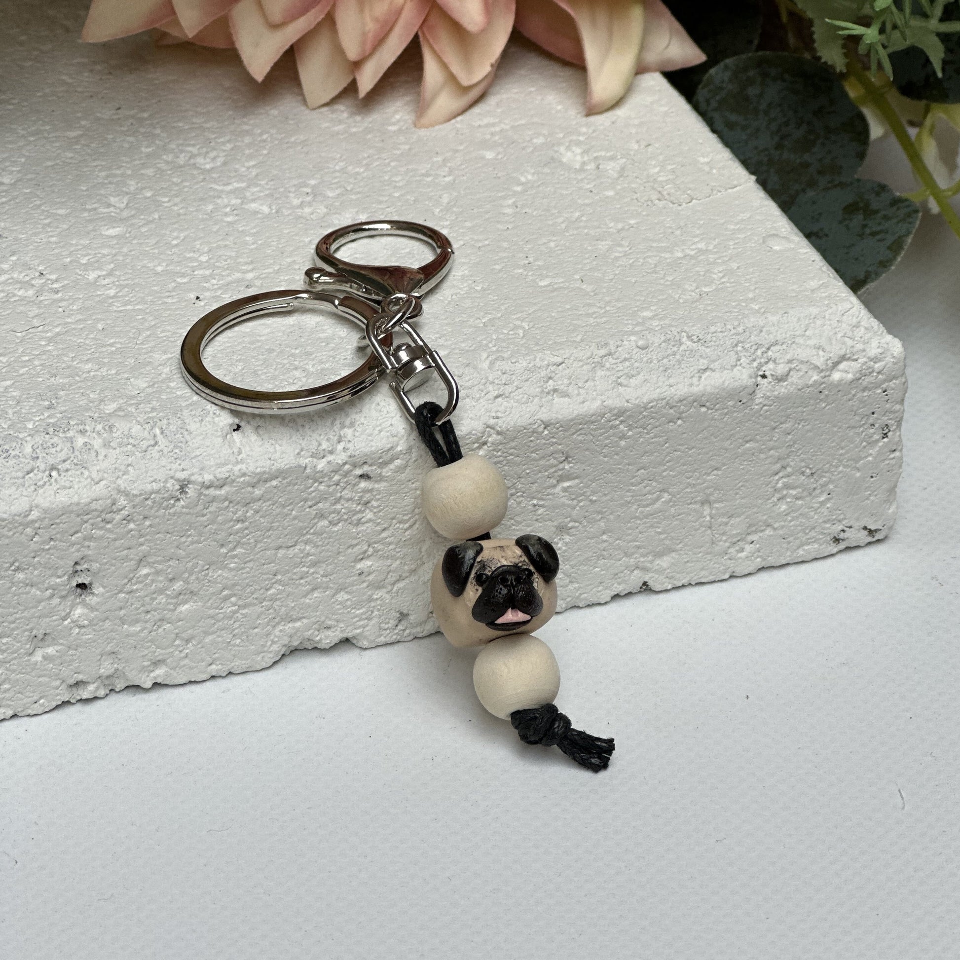 Handmade pug polymer clay and timber keying on white textured background with a pink flower in the background