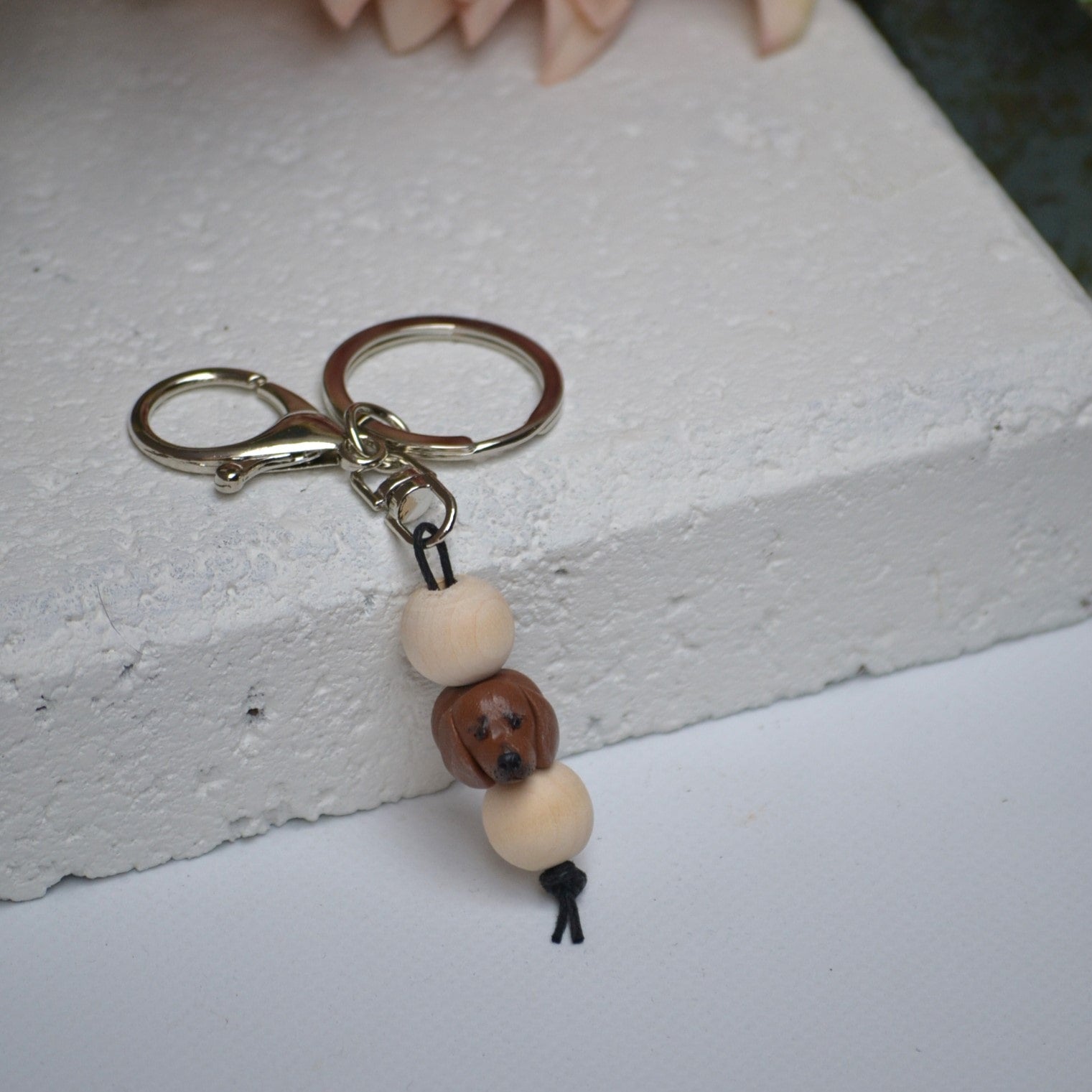 Handmade dachshund polymer clay and timber keying on white textured background with a pink flower in the background