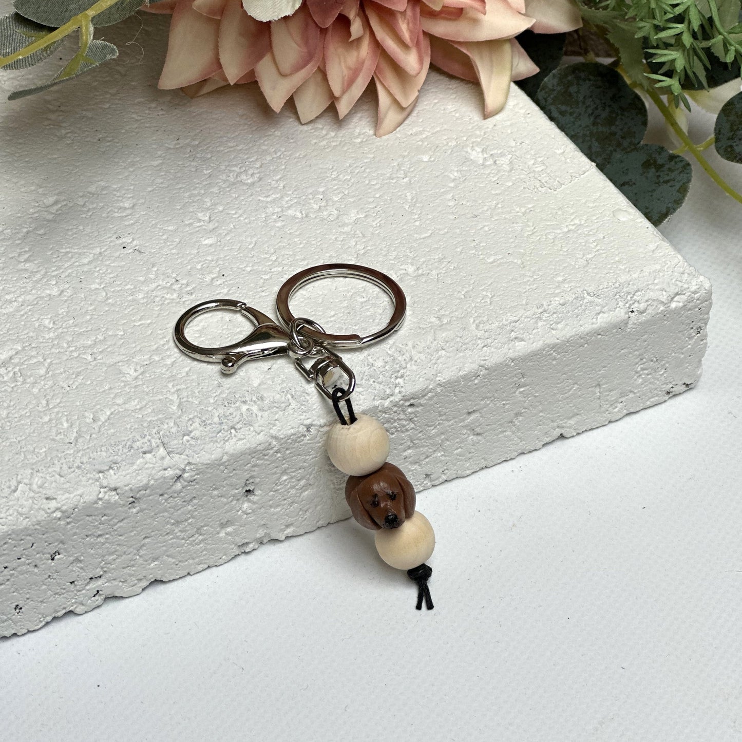 Handmade dachshund polymer clay and timber keying on white textured background with a pink flower in the background