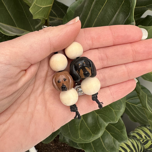 Hand holding two dachshund dog-shaped beads on a string with a green leafy background