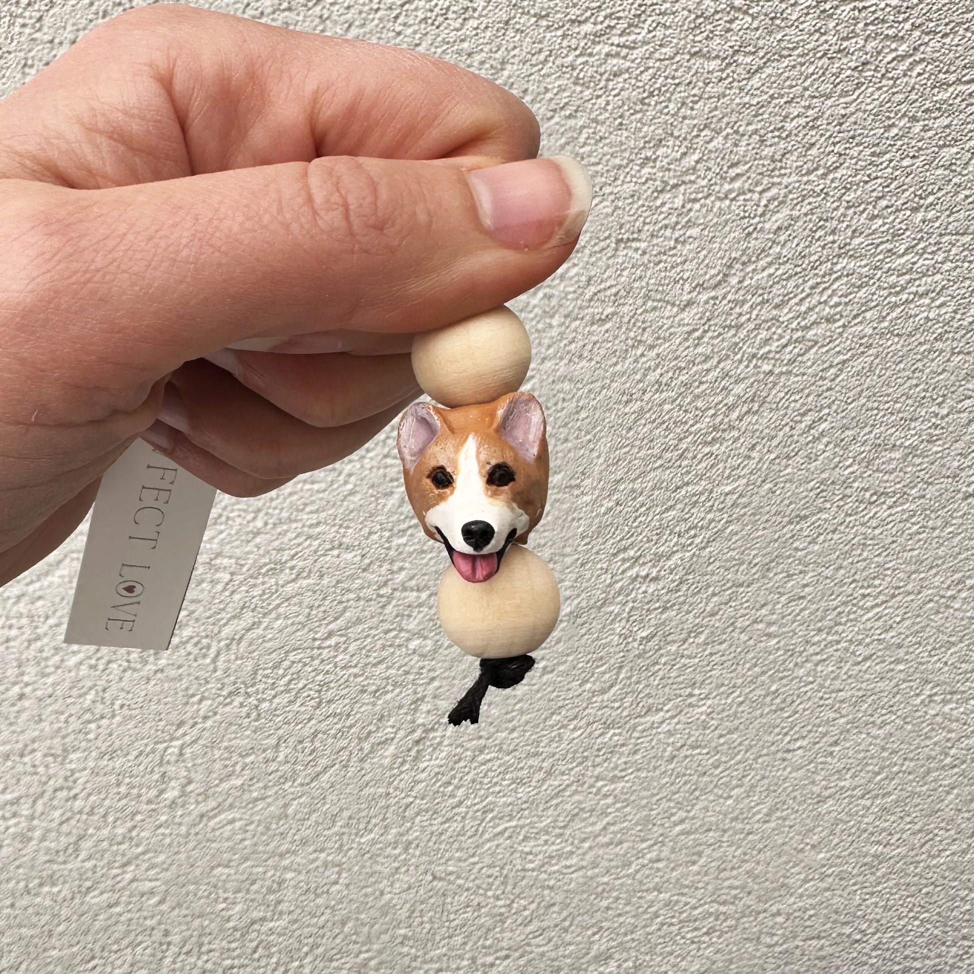 Hand holding a small corgi dog keyring with a plain background